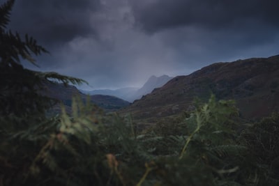 绿色草地附近的山在灰色的云层
